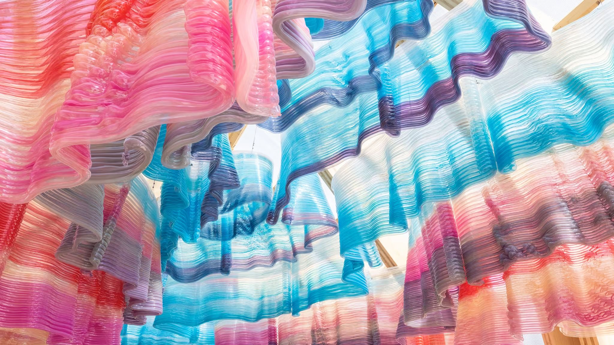Looking up into a cupola of ruffled, translucent plastic layers in pink, blue and purple, printed as hollow tubular beads