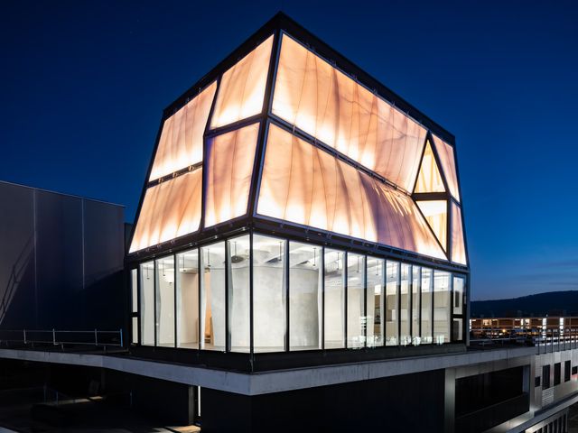 The upper floors of DFAB HOUSE at night, a faceted translucent facade glowing above a glazed storey
