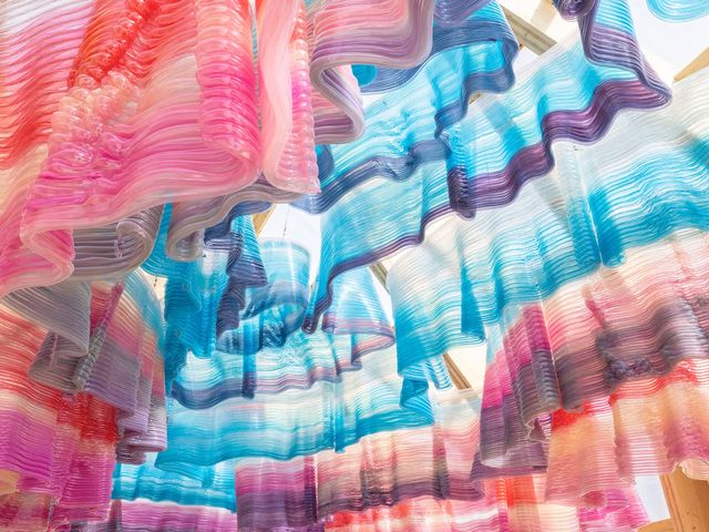 Looking up into a cupola of ruffled, translucent plastic layers in pink, blue and purple, printed as hollow tubular beads