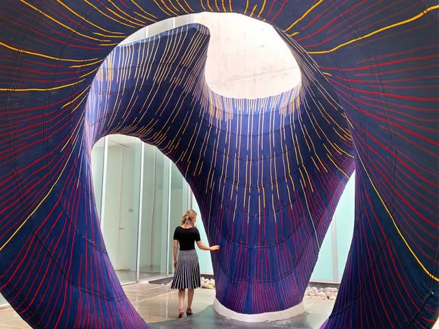 A woman standing inside a sweeping concrete shell lined with a purple knitted textile