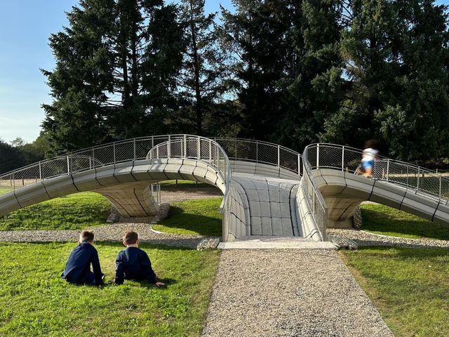 Two people sitting on the grass in front of a curving concrete footbridge with steel railings